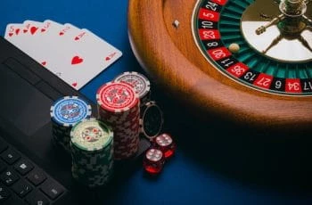 Zylinder eines Rouletterades, Karten und Pokerchips neben einem Laptop.